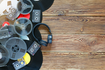 Old vintage bobbins, vinyl records, cassette tapes and headphones on a wood table background. Multicolored labels. Top view. Place to copy space. Sun glare.