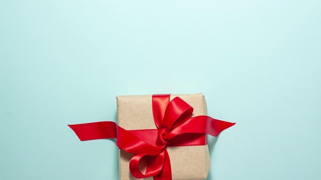 Brown paper gift box with a red ribbon bow fall down on blue background. Flat lay top view stop motion animation with copyspace