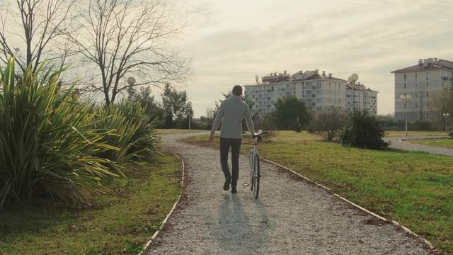 A man with a Bicycle walks through the autumn Park on a Sunny day. Rear view. A traking shot.