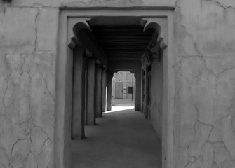 Fototapeta premium Through Passage with access to the Sunny street and the house opposite in an old stone building with columns and arches in the Arabic style black and white