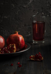 Two pomegranates lie on a metal plate, which stands on a dark wooden table. About them is part of...