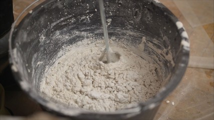 Builder mixing plaster in a bucket using an electric mixer. Builder mixes the mixture in a bucket using a construction mixer