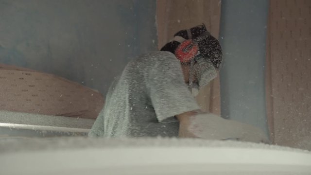 Sequence of shots of professional surfboard shaper wearing protective equipment working in workshop