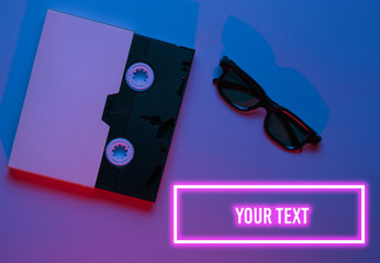 Video cassette in cover, 3D glasses. 80s. Retro wave, blue red neon light, ultraviolet. Top view, minimalism