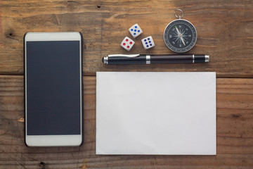 Wooden background desk with paper,dice,compass,smart phone and pen.Top view with copy space