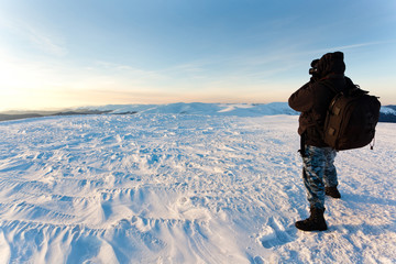 Young man photographer in winter clothing standing and making photo in sunlight