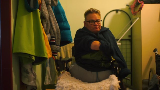 A disabled person takes off his sweater in the hallway of the apartment.