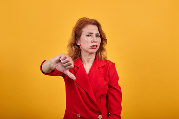 Disappointed caucasian young woman wearing fashion red jacket over isolated orange background pointing thumbs down. People lifestyle concept.