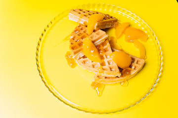Waffles with peaches for breakfast on a yellow background. 
