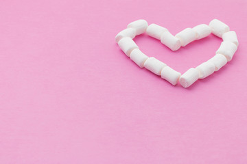 a shape of heart made of small marshmallows on a pink background, low view