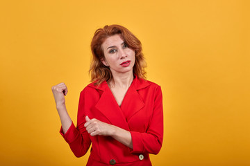 Naklejka premium Disappointed caucasian young woman pointing thumbs behing back, looking at camera wearing fashion red jacket over isolated orange background. People lifestyle concept.