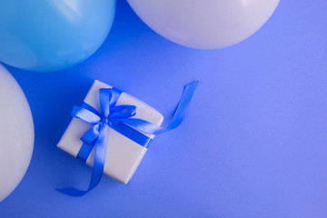Gift with blue bow, blue and white balloons on the blue  background. Top view. Copy space.