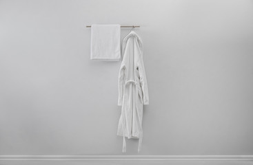 Rack with clean bathrobe and towel on light wall