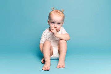 baby girl sits on the floor and sucks a finger