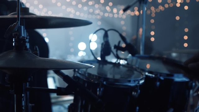 Close up of the hands of a drummer with a stick. The group performs on stage. A man plays the drums in a musical group, live performance. Drummer on stage. Close the drum cymbals and drummer's hands.