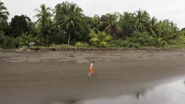 Aerial follows a young man jogging at an empty beach in Choco, Colombia.