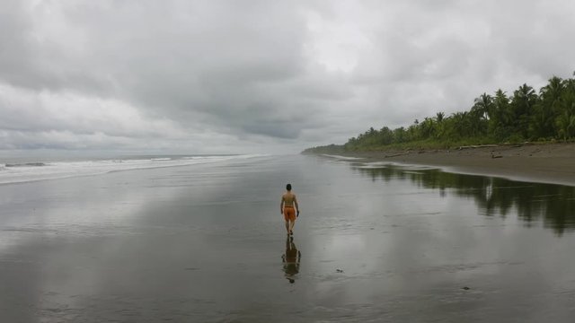 Aerial follows a young man from behind, walking at an empty beach in Nuqui, Colombia.