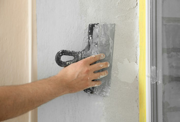 Man plastering window area with putty knife indoors, closeup. Interior repair