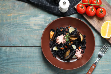 Delicious black risotto with seafood served on blue wooden table, flat lay