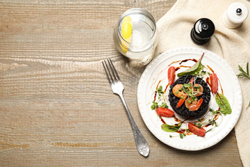 Delicious black risotto with seafood served on wooden table. Space for text