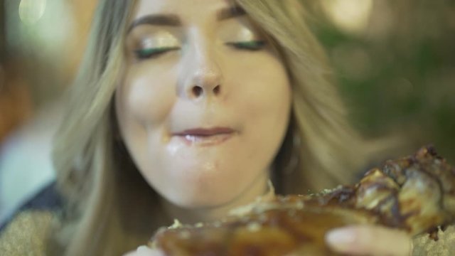 Beautiful blonde young greedy woman biting huge pieces of meat eating with hands angry inappropriate in close up view