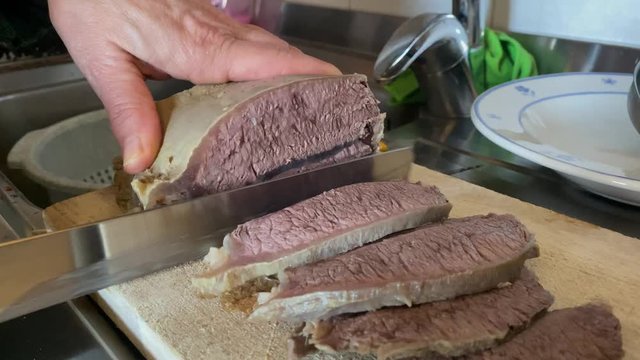 Treviglio,Italia, 25 Dicembre 2019, una donna taglia un pezzo di carne di manzo bollita in tante piccole fette sopra un tagliere di legno