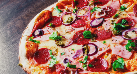 Pizza with Mozzarella cheese, ham, tomato sauce, salami, onion, pepper, Spices and Fresh basil. Italian pizza on wooden table background