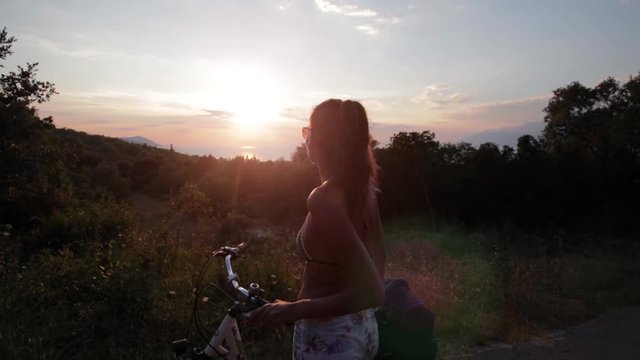 Young woman taking a break from cycling to enjoy the beautiful sunset on the island of Hvar