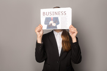businesswoman obscuring face with business newspaper isolated on grey