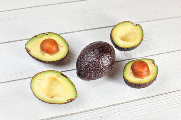 Avocado halves, and one whole fruit arranged on white boards desk