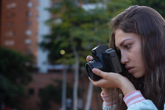 Mujer joven fotografiando en el parque con su camara reflex antigua