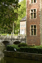 Un coin du château avec l'une de ses dépendances et le pont en pierres sous la nature luxuriante du domaine Coloma à Sint-Pieter-Leeuw