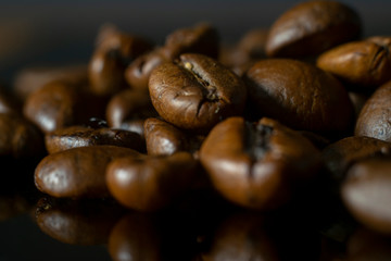 Fresh fragrant coffee grains close-up on black glass. Macro photography.
