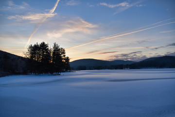 Cold Sunrise Over Tree Covered Hills And Frozen Water With Snow At Red House Lake, Allegany State Park, New York