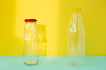 Glass bottle for drinks with a red cap and a plastic bottle on a yellow-blue background. An example of packaging that is healthy and environmentally friendly and then properly recycled and disposed of