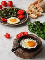 Delicious fried eggs in a pan with fried spinach and mushrooms located on a gray table. Close-up. Vertical orientation.