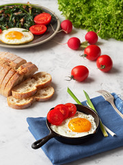 Delicious fried eggs in a pan with fried spinach and mushrooms located on a gray table. Close-up. Vertical orientation.
