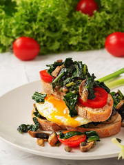 Toast with scrambled eggs on toasted bread with spinach, mushrooms and tomato on a gray plate. Close-up. Fried egg for breakfast. Vertical orientation.