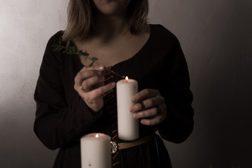 A woman dressed in a medieval dress holds a burning white candle in her hand. Mystery witch