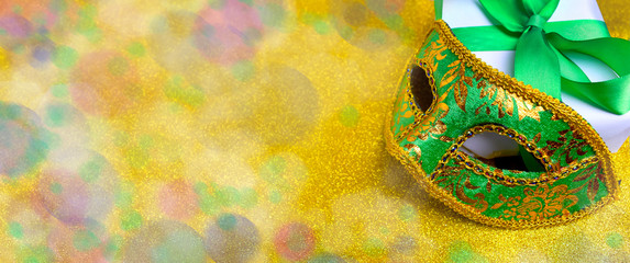 Ornate carnival mask, gift box on bokeh lights glitter golden background. Mardi gras festive celebration banner with copy space. © Olga