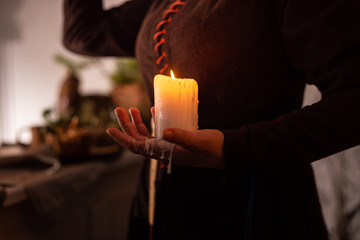 A woman dressed in a medieval dress holds a burning white candle in her hand. Mystery witch