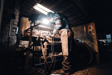 In the dark metal factory busy man is working on his workplace.