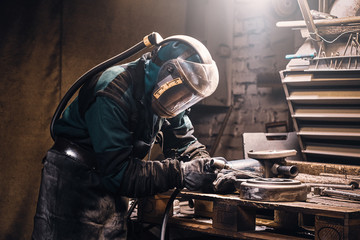 Diligent worker in protective mask making welding while working at his workplace.