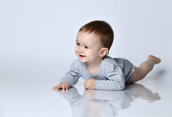 Little baby boy toddler in grey casual jumpsuit and barefoot lying on floor, smiling and looking up