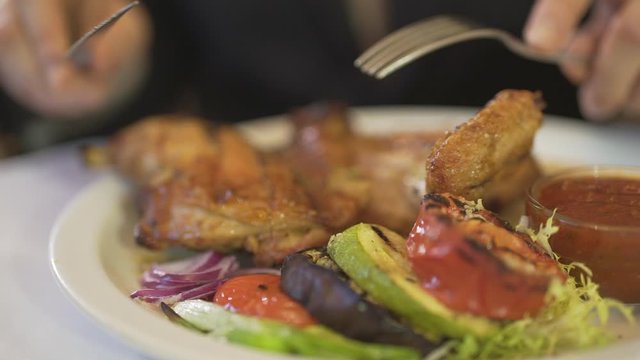 Close up view on man hand with fork knife cut delicious griller vegetable fried chicken meat meal in fancy restaurant