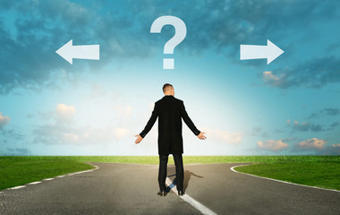 Confused businessman standing at crossroads with arrows and question mark. Concept of choice