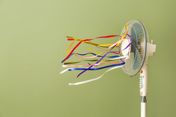 Electric fan with fluttering ribbons on color background