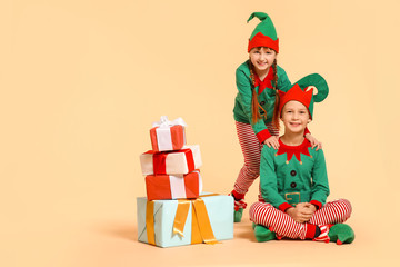 Little children in costume of elf and with gifts on color background