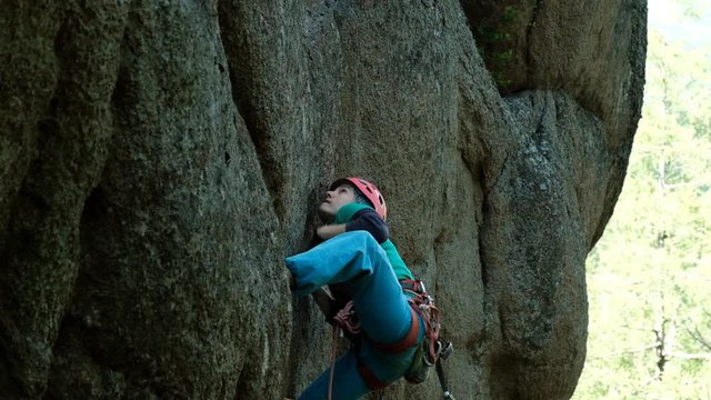 A young woman climbs a difficult route on a vertical wall.
