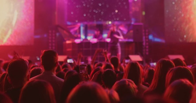 Artist performs on stage, a crowd of spectators looks out of the hall. Concert of a popular artist, the audience shoot a concert on a smartphone.